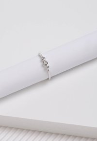 Silberring mit drei runden klaren Steinen, die in einem schlanken Band eingefasst sind, auf einer strukturierten weißen Oberfläche ruhend.