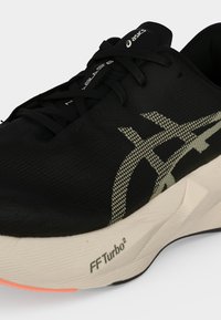 Μαύρο αθλητικό παπούτσι Asics με μπεζ λογότυπο, λευκή σόλα με την ένδειξη FF Turbo² και μαύρα κορδόνια σε απλό φωτεινό φόντο.