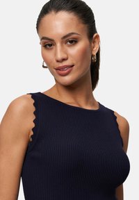 Débardeur rayé marine avec des détails à volants aux épaules. Fabriqué en matériau extensible, sa coupe ajustée met en valeur la forme et la texture.