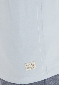 Tricou din bumbac de culoare bleu deschis, cu mâneci scurte, având o margine cusută și un mic eticheta a brandului în colțul din stânga jos.