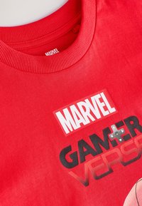 T-shirt di cotone rosso con colletto a girocollo a coste. La grafica stampata include "MARVEL" e "GAMERVERSE" in colori audaci e a contrasto.