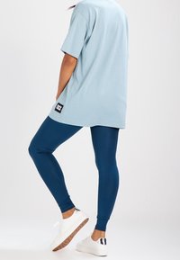 Camiseta de gran tamaño azul claro con un parche de logo, combinada con leggings ajustados azul marino y zapatillas blancas con detalles plateados.