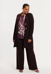 Burgundy long jacket with gold buttons over a purple graphic top featuring a white floral design and wide-leg pants. Smooth fabric texture.
