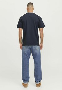 Camiseta de algodón azul marino con un corte relajado, mangas cortas y cuello redondo, combinada con jeans de denim azul claro y calzado marrón.