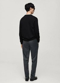 Svart tröja med rund hals, grå skräddarsydda byxor och svarta skor. Den bakre vyn visar en minimalistisk design och en ren silhuett.