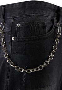 Los pantalones de mezclilla negra presentan un cinturón lateral de cadena en metal plateado, con un bolsillo trasero visible y sutiles variaciones de textura en la tela.