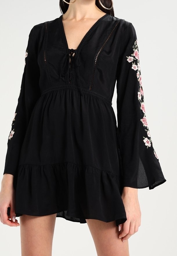 Svart långärmad klänning med V-ringning, blommig brodyr på ärmarna, en åtsittande korsett och en utsvängd, tärnad fåll. Mjuk tygkänsla.