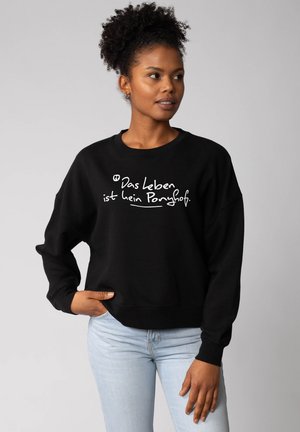 Black sweatshirt with a loose fit featuring white text “Das leben ist kein Ponyhof” on the front. Constructed from soft, textured fabric.