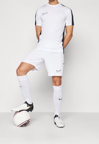Vitt Nike fotbollskit med svarta accenter, bestående av en kortärmad tröja och shorts. Spelaren står med en svart och vit fotboll.