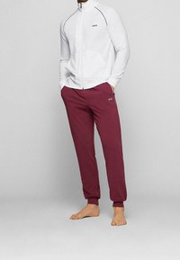 Tuta sportiva con giacca bianca con zip e pantaloni jogger color bordeaux, entrambi con il logo "BOSS". Tessuto morbido e vestibilità comoda.