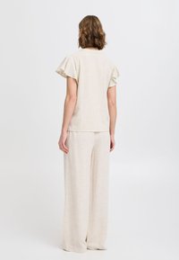 Top in lino beige chiaro con maniche corte a volant, abbinato a pantaloni a gamba larga nello stesso tessuto, creando un insieme coeso e texturizzato.