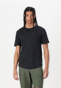 Schwarzes Baumwoll-T-Shirt mit kurzen Ärmeln, rundem Halsausschnitt und lockerer Passform, kombiniert mit olivgrünen Shorts. Keine auffälligen Muster oder Grafiken.