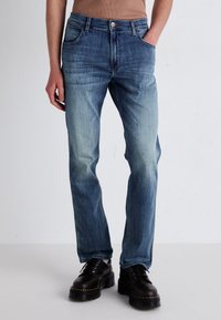 Jeans de denim azul claro con un diseño de pierna recta, textura deslavada, cinco bolsillos y detalle del botón superior, combinados con botas negras de cordones.