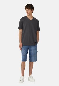 Czarny t-shirt z dekoltem w serek, niebieskie dżinsowe szorty do kolan z detalami szycia oraz białe sneakersy. Prosty, codzienny strój casualowy.