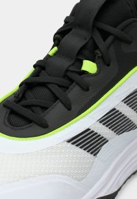 Αθλητικό παπούτσι με ανάγλυφο μαύρο επάνω μέρος, πράσινες λεπτομέρειες, λευκή ενδιάμεση σόλα και ρίγες σε μαύρο και λευκό στο πλάι.