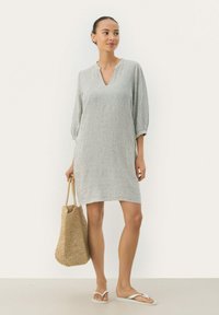 Gestreiftes, knielanges Kleid mit V-Ausschnitt und Dreiviertelärmel, aus leichtem Stoff gefertigt. Kombiniert mit einer gewebten Tasche und Flip-Flops.