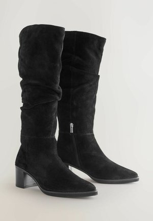 Schwarze Wildleder-Stiefel in knöchelhoher Länge mit einem lässigen Design, quadratischer Zehenform und Blockabsatz. Verfügt über einen silbernen Seitenreißverschluss zur Sicherung.