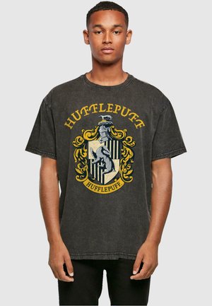 Schwarzes Baumwoll-T-Shirt mit einem Hufflepuff-Wappen in Gelb und Grau, mit detaillierten Grafiken und einem runden Ausschnitt. Kurze Ärmel.