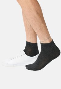 Nilkkasukat tummanharmaana, valmistettu pehmeästä, joustavasta materiaalista, valkoisen lenkkarin kanssa kontrastina. Varret ovat resorilliset ja mallissa on minimalistinen design.