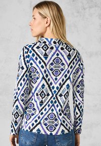 Langsamige top met een ruitpatroon in het wit, blauw en paars. De stof heeft een gladde textuur met contrasterende zwarte accenten.