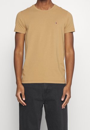 T-shirt en coton beige à manches courtes avec un col rond, présentant un petit logo brodé sur la poitrine et une silhouette ajustée.