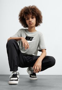 Pilkas trumpomis rankovėmis marškinėliai su juodu Nike logotipu, derinami su juodomis aptemptomis kelnėmis ir juodai baltais sportbačiais. Lygus audinys, laisvas kirpimas.
