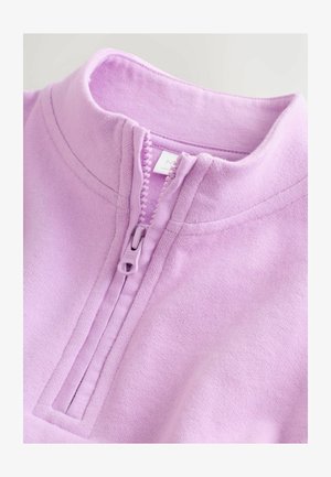 Svijetlo ljubičasta majica s okovratnikom na patentni zatvarač od mekog materijala. Ima glatku teksturu, uspravni ovratnik i kratki patentni zatvarač s okruglom kopčom.