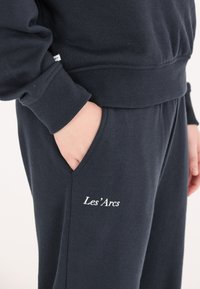 Mörkblå sweatshirt och byx-set i mjukt tyg, med en ficka och broderad "Les'Arcs" detalj. Mudden och midjebandet är ribbstickade.