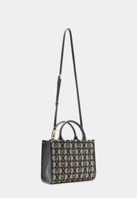 Handtasche aus gemustertem beigem Stoff mit schwarzen Akzenten, doppelten Griffen und einem abnehmbaren schwarzen Schulterriemen. Strukturierte Oberfläche. 