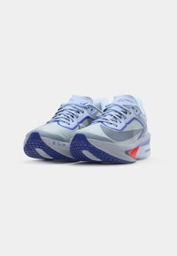 Zapatillas de deporte azul claro con parte superior de malla, suela curva y acentos morados. Presentan una suela exterior con agarre texturizado y cordones en la parte delantera.