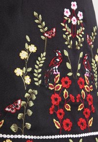 Czarna tkanina z kolorowymi haftowanymi wzorami kwiatów i ptaków. Zawiera czerwone, żółte i zielone elementy z misternym zdobieniem i teksturą.