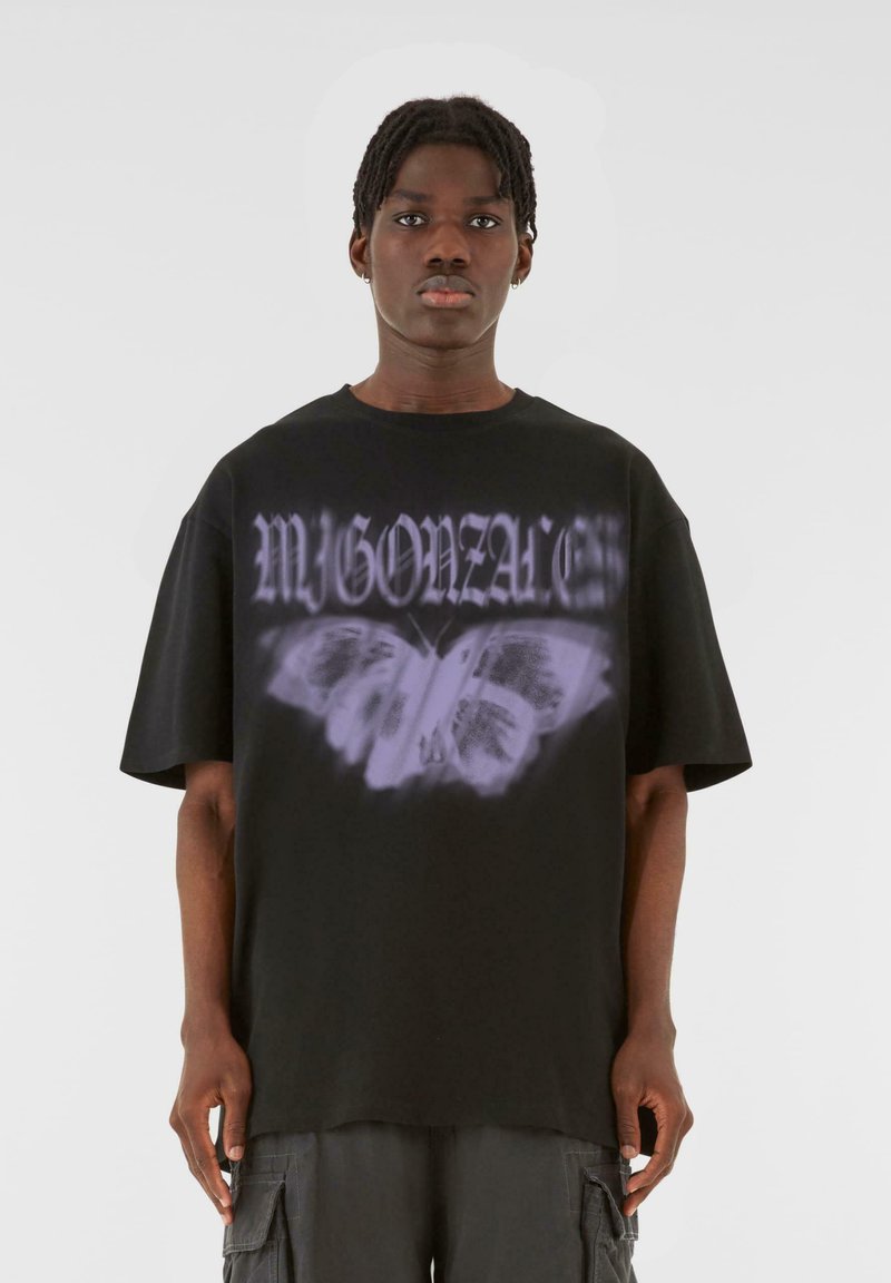 Svart oversized T-shirt i bomull, med en vit och lila fjärilsdesign och stiliserad text ovanför, korta ärmar och rund halsringning.