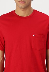 T-shirt en coton rouge à manches courtes, col rond et poche sur la poitrine gauche arborant un petit logo en bleu, blanc et rouge.