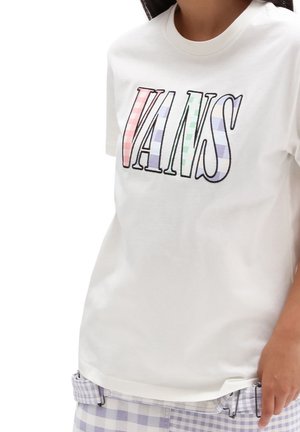Chemise blanche à manches courtes avec de grandes lettres rayées colorées "VANS" portée par une personne au teint moyen et aux longs cheveux foncés.