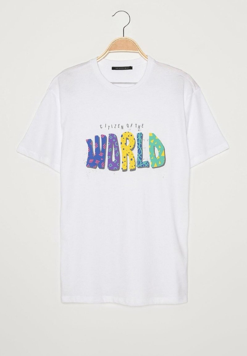 T-shirt blanc à manches courtes sur un cintre en bois avec le texte coloré « CITOYEN DU MONDE » en lettres ludiques et à motifs, centré sur le devant.