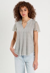 Blouse à manches courtes en crème avec un motif géométrique, dotée d'un décolleté en V et d'un design plissé. Fabriquée en tissu léger et texturé.