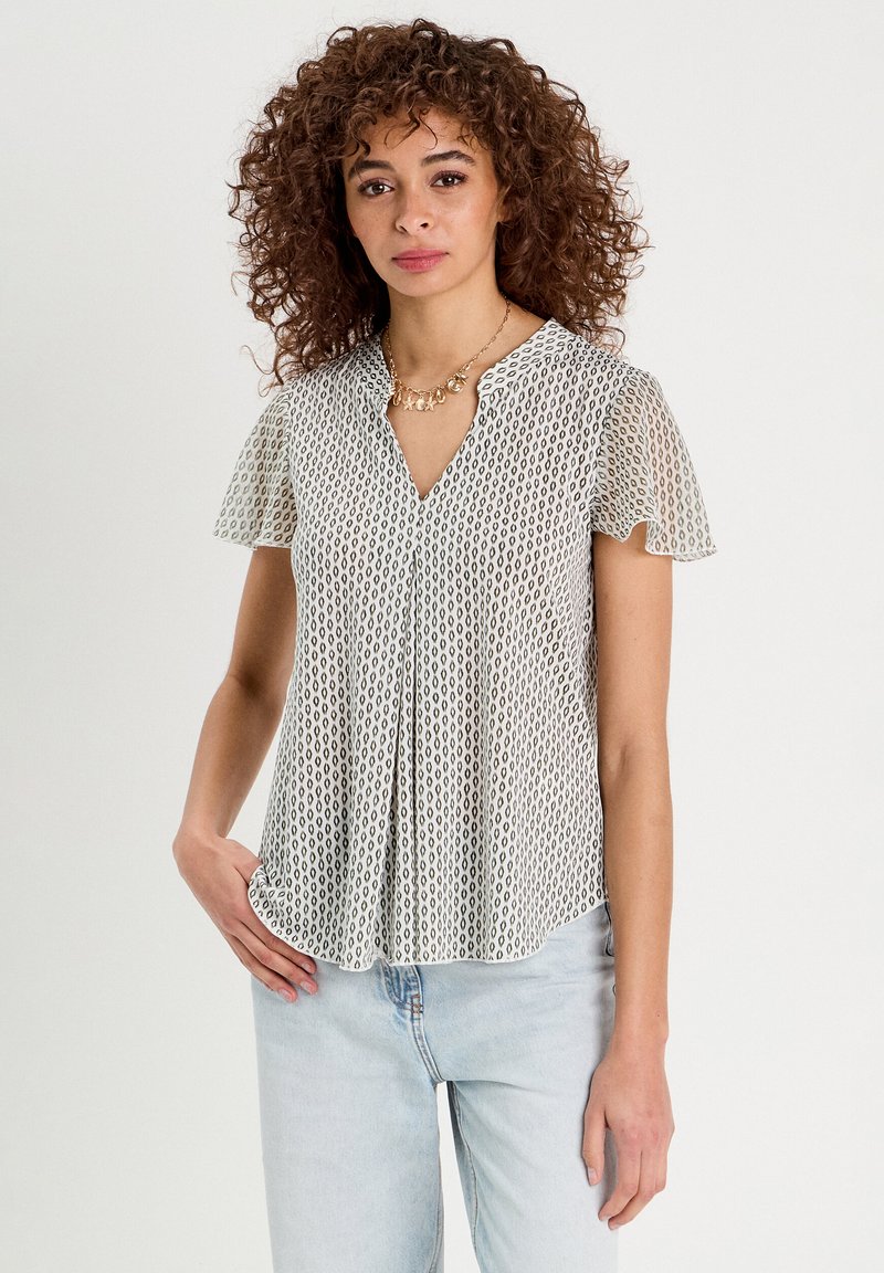 Blouse à manches courtes en crème avec un motif géométrique, dotée d'un décolleté en V et d'un design plissé. Fabriquée en tissu léger et texturé.