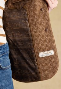 Veste en tweed chevron marron avec illustrations imprimées d'équitation sur la doublure intérieure sombre et étiquette « Joules Tweed » dans la poche intérieure.