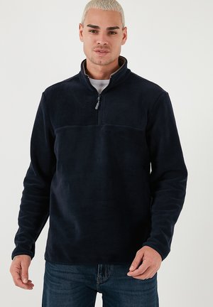 Sudadera de felpa azul marino con cuello de cremallera hasta el cuarto, textura suave, mangas largas y una costura horizontal en el pecho.