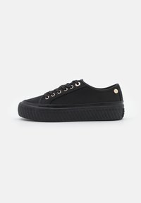 Czarne niskie sneakersy z teksturowaną gumową podeszwą, materiałowym wierzchem, czarnymi sznurówkami i małym okrągłym metalowym logo w pobliżu pięty.