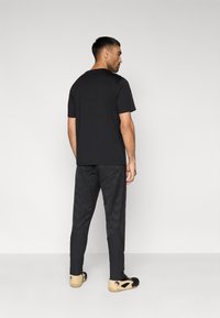 Μαύρο κοντομάνικο T-shirt με υφασματικές λεπτομέρειες στους ώμους και μαύρο ψηλόμεσο παντελόνι με γεωμετρικό σχέδιο. Τα παπούτσια είναι μαύρα με μπεζ λεπτομέρειες.