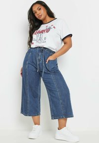 White t-shirt with navy trim featuring a graphic print. High-waisted, wide-leg denim pants, mid-blue, with drawstring and side pockets.