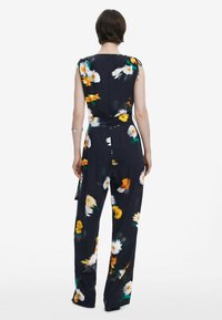 Marint blommig jumpsuit med ärmlös design, prydd med gula och vita tusenskönor, dragband i midjan och bred benprofil.