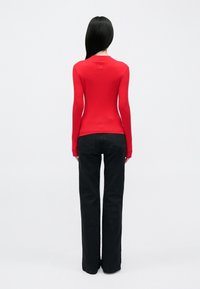 Piros bordázott hosszú ujjú felső fekete, bővülő farmerral párosítva, testhez simuló szabással, texturált anyaggal és magas nyakkal.