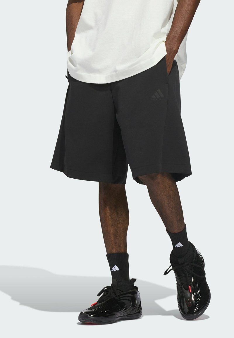 Pantalones cortos deportivos negros con un corte holgado y cintura elástica, con un sutil logo de Adidas. Usados con zapatillas y calcetines negros.