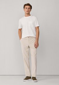 Camiseta blanca de algodón con un bolsillo en el pecho, combinada con chinos beige claros y zapatillas de ante marrón. Atuendo simple y casual.