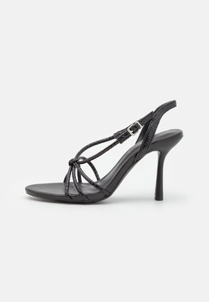 Sandale noire à talon haut avec fines brides tressées, fermeture à boucle et talon stiletto fin sur fond uni.