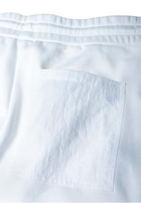 Shorts blancs avec un tissu texturé, une ceinture élastique avec un détail de couture, et une poche plaquée carrée à l'arrière.