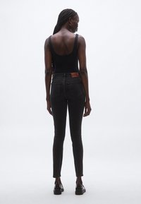 Vaqueros negros de talle alto con una textura suave, que cuentan con un parche de cuero marrón en la parte trasera y un ajuste ceñido y cónico.