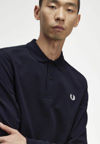 Tumed sinine polo särk tekstureeritud kangaga, klassikaline krae, kolm nuppu ja vasakul rinnal välja tikitud logo.